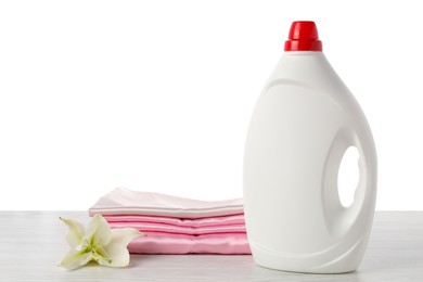 Photo of Bottle of fabric softener, stacked clothes and flower on wooden table against white background