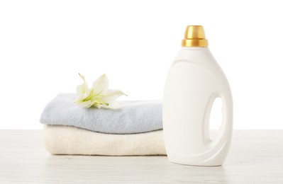 Photo of Bottle of fabric softener, stacked clothes and flower on wooden table against white background
