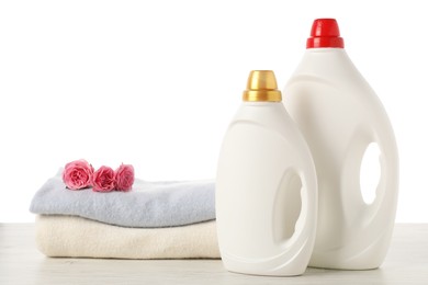 Photo of Bottles of fabric softener, stacked clothes and flowers on wooden table against white background