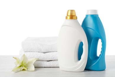 Photo of Bottles of fabric softener, stacked towels and flower on wooden table against white background