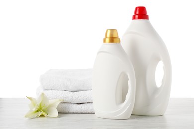 Photo of Bottles of fabric softener, stacked towels and flower on wooden table against white background