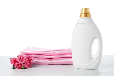 Photo of Bottle of fabric softener, stacked clothes and flowers on marble table against white background