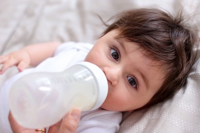 Photo of Father feeding his little baby with bottle on bed at home, closeup