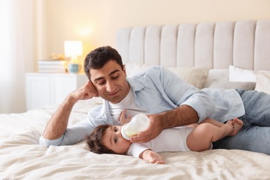Photo of Father feeding his little baby with bottle on bed at home