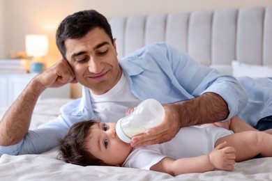 Photo of Father feeding his little baby with bottle on bed at home