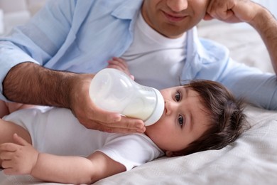 Photo of Father feeding his little baby with bottle on bed at home, closeup