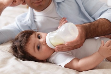 Photo of Father feeding his little baby with bottle on bed at home, closeup