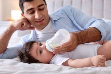 Photo of Father feeding his little baby with bottle on bed at home
