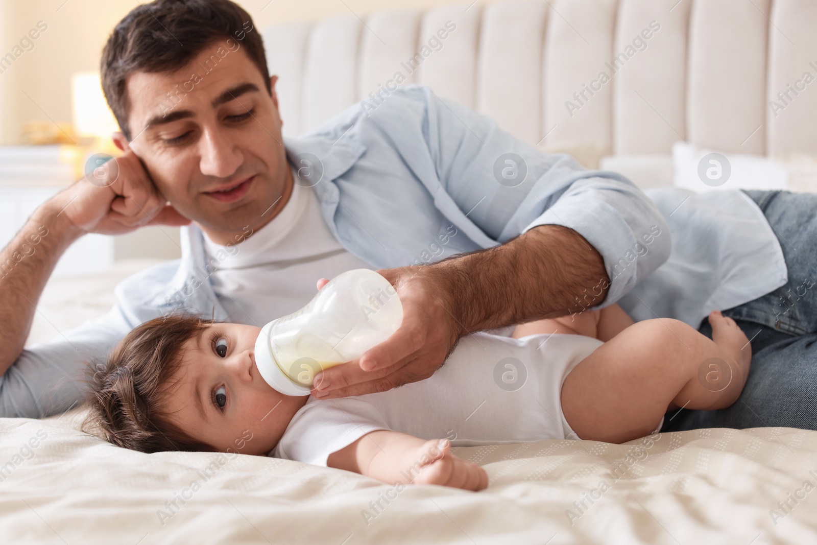 Father feeding his little baby with bottle on bed at home Photo of Father feeding his little baby with bottle on bed at home