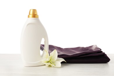 Photo of Bottle of fabric softener, stacked clothes and flower on wooden table against white background