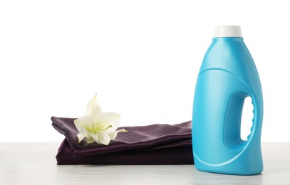 Photo of Bottle of fabric softener, stacked clothes and flower on wooden table against white background