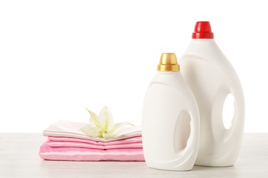 Photo of Bottles of fabric softener, stacked clothes and flower on wooden table against white background