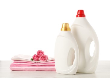 Photo of Bottles of fabric softener, stacked clothes and flowers on wooden table against white background