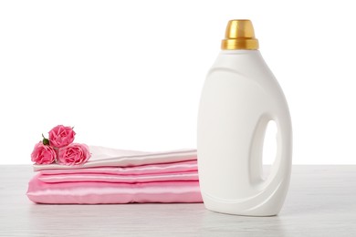 Photo of Bottle of fabric softener, stacked clothes and flowers on wooden table against white background
