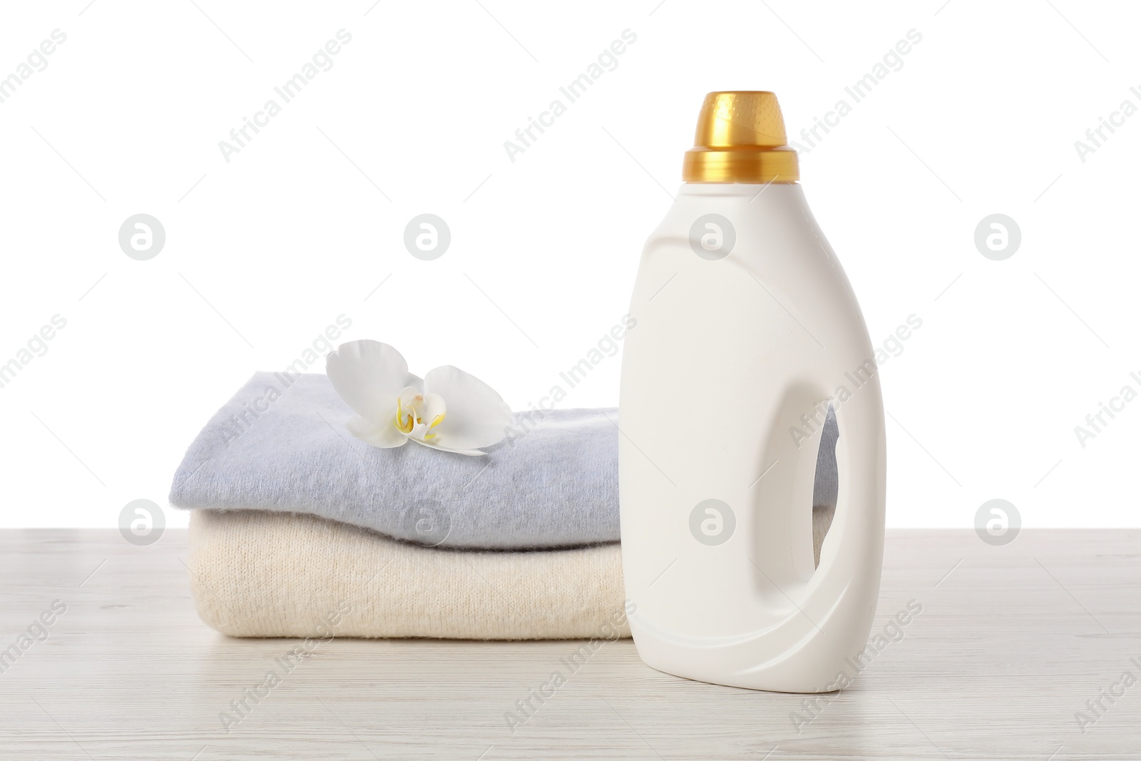 Bottle of fabric softener, stacked clothes and flower on wooden table against white background Photo of Bottle of fabric softener, stacked clothes and flower on wooden table against white background