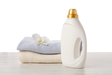 Photo of Bottle of fabric softener, stacked clothes and flower on wooden table against white background