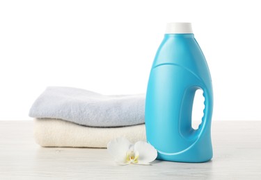Photo of Bottle of fabric softener, stacked clothes and flower on wooden table against white background
