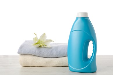 Photo of Bottle of fabric softener, stacked clothes and flower on wooden table against white background