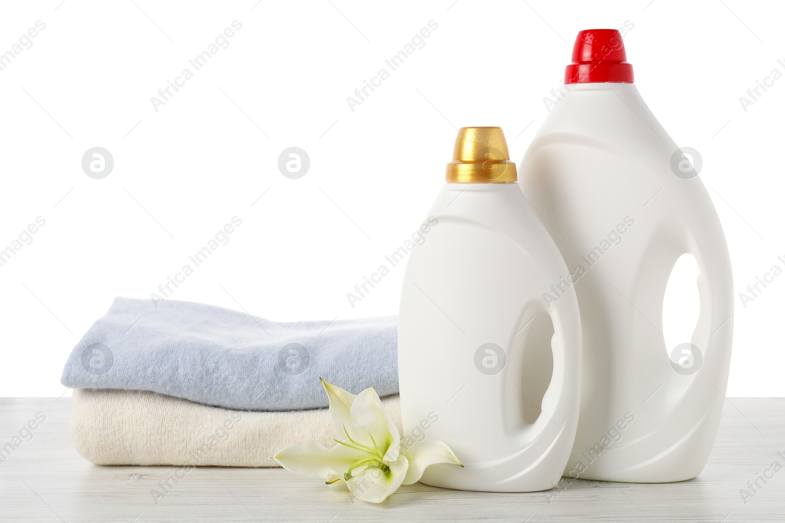 Bottles of fabric softener, stacked clothes and flower on wooden table against white background Photo of Bottles of fabric softener, stacked clothes and flower on wooden table against white background