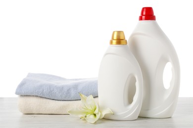 Photo of Bottles of fabric softener, stacked clothes and flower on wooden table against white background