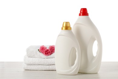 Photo of Bottles of fabric softener, stacked towels and flowers on wooden table against white background