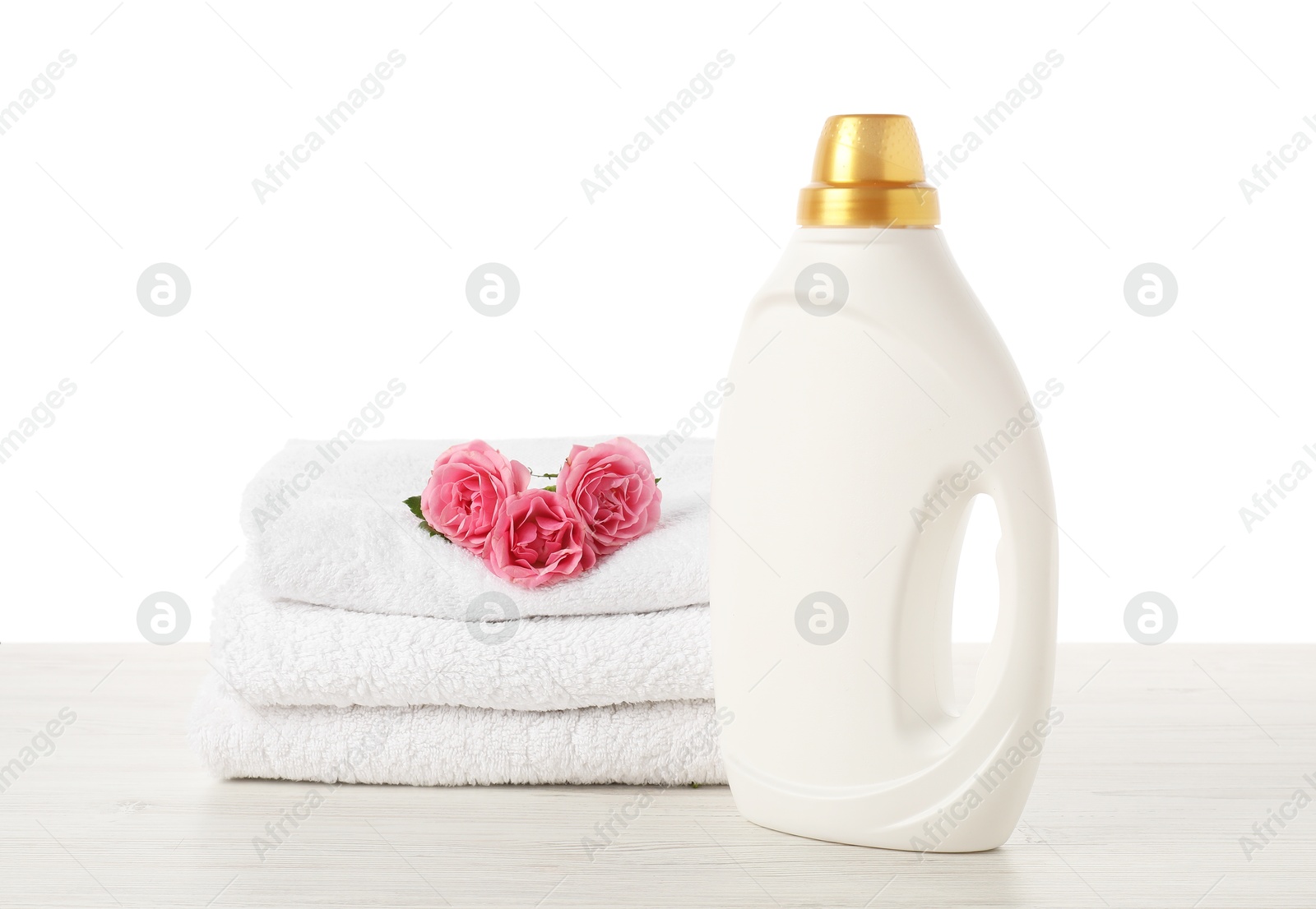 Bottle of fabric softener, stacked towels and flowers on wooden table against white background Photo of Bottle of fabric softener, stacked towels and flowers on wooden table against white background