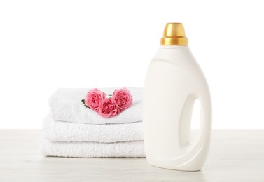 Photo of Bottle of fabric softener, stacked towels and flowers on wooden table against white background