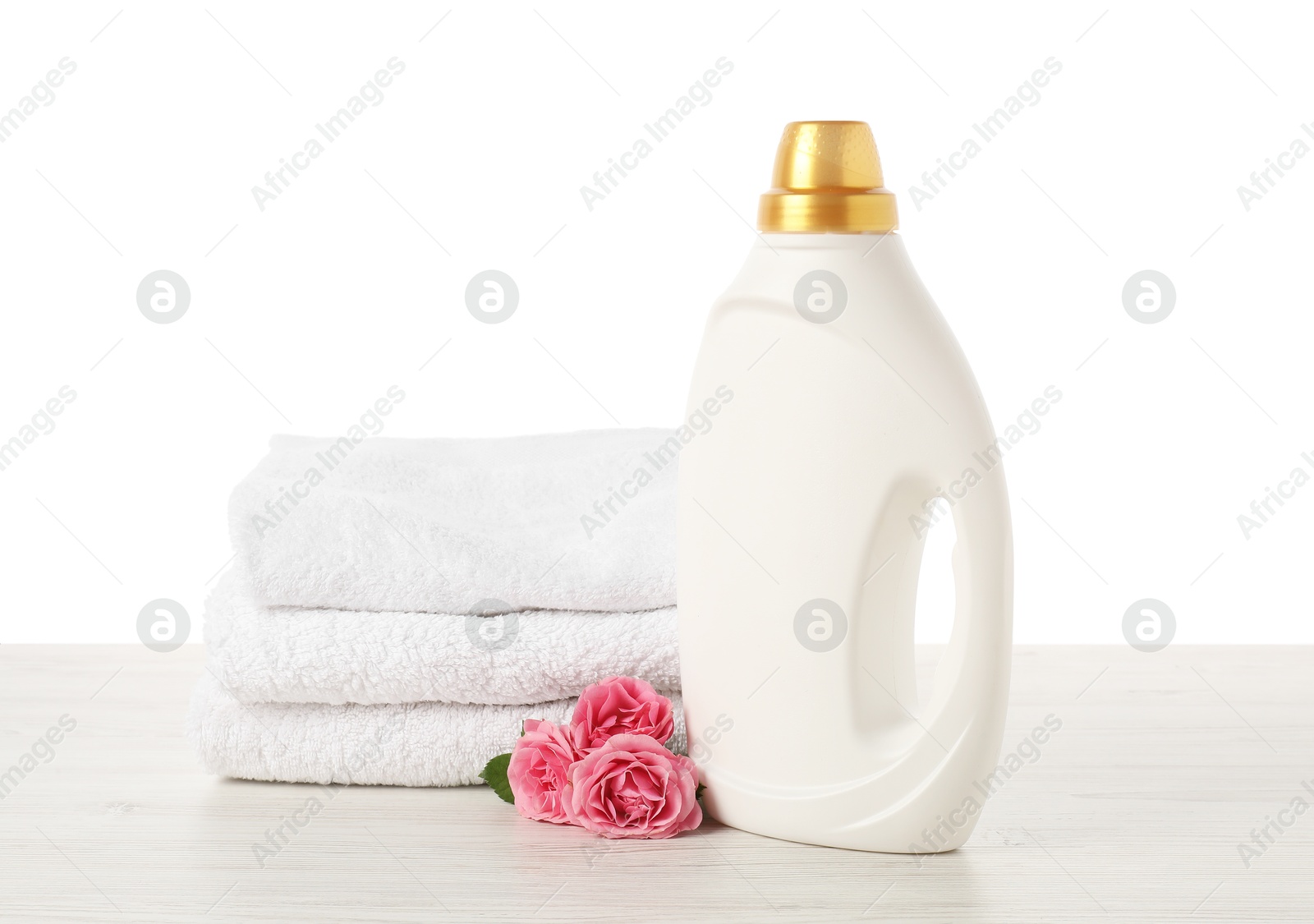 Bottle of fabric softener, stacked towels and flowers on wooden table against white background Photo of Bottle of fabric softener, stacked towels and flowers on wooden table against white background