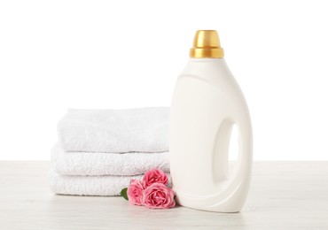 Photo of Bottle of fabric softener, stacked towels and flowers on wooden table against white background