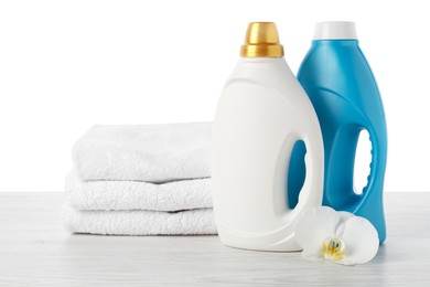 Photo of Bottles of fabric softener, stacked towels and flower on wooden table against white background
