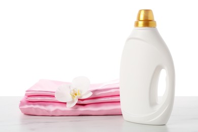 Photo of Bottle of fabric softener, stacked clothes and flower on marble table against white background