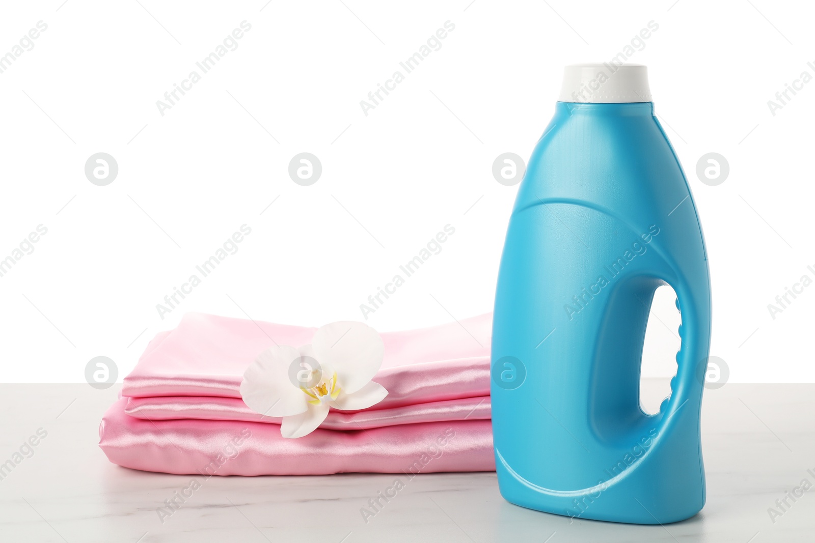 Bottle of fabric softener, stacked clothes and flower on marble table against white background Photo of Bottle of fabric softener, stacked clothes and flower on marble table against white background