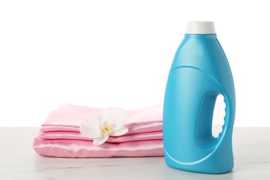 Photo of Bottle of fabric softener, stacked clothes and flower on marble table against white background