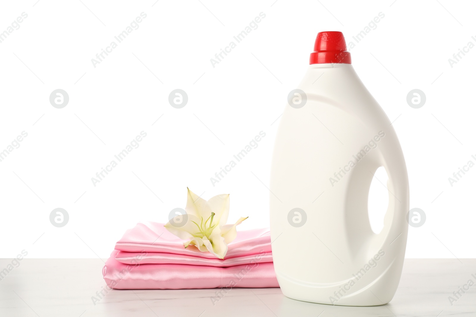 Bottle of fabric softener, stacked clothes and flower on marble table against white background Photo of Bottle of fabric softener, stacked clothes and flower on marble table against white background