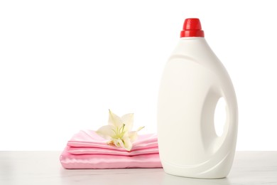 Photo of Bottle of fabric softener, stacked clothes and flower on marble table against white background
