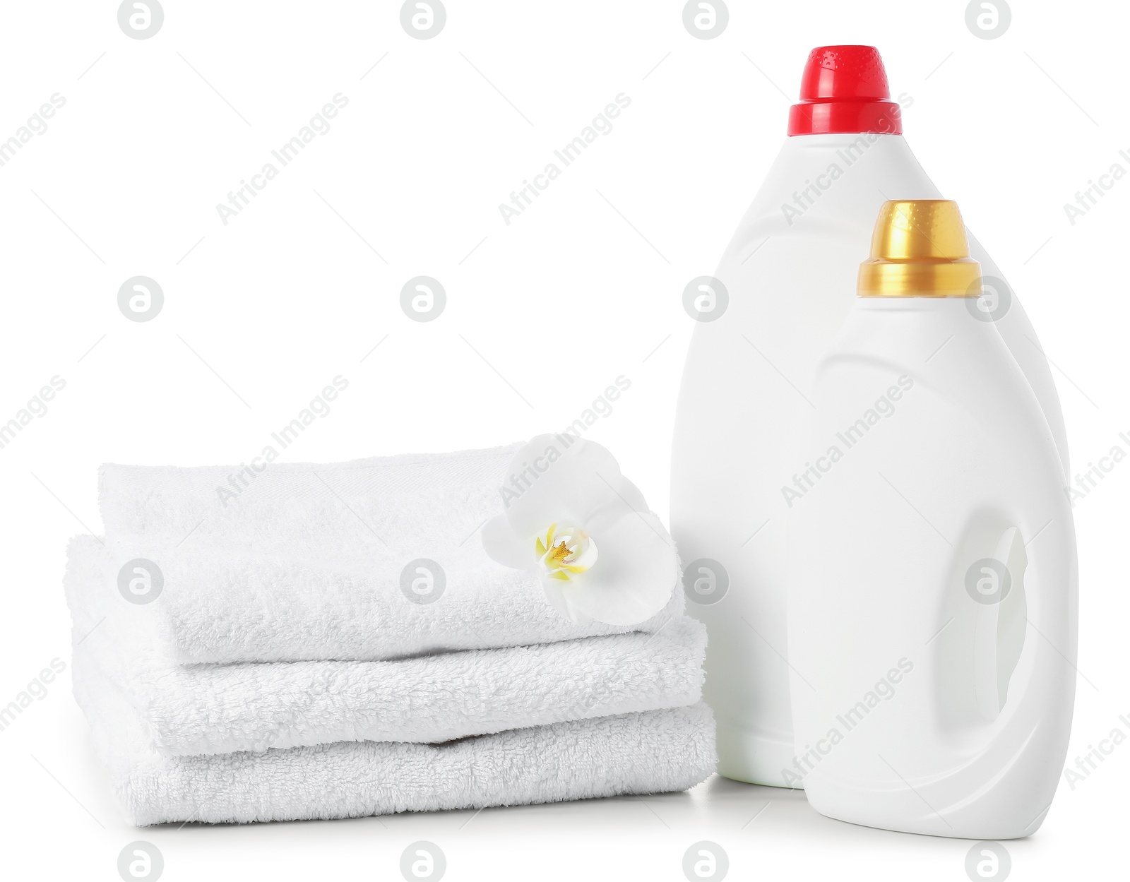 Bottles of fabric softener, stacked towels and flower isolated on white Photo of Bottles of fabric softener, stacked towels and flower isolated on white