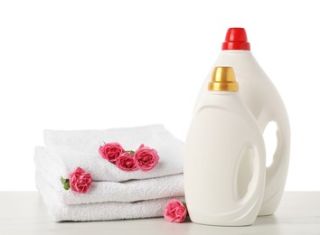 Photo of Bottles of fabric softener, stacked towels and flowers on marble table against white background