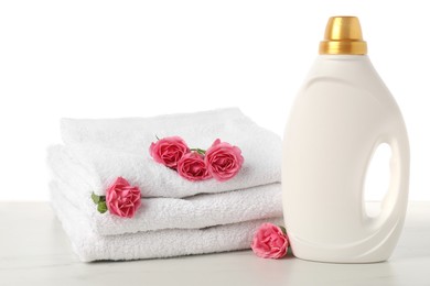 Photo of Bottle of fabric softener, stacked towels and flowers on marble table against white background