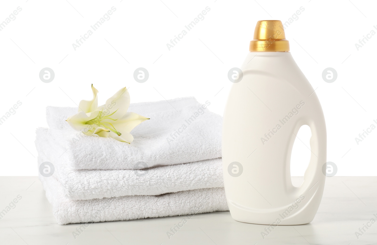 Bottle of fabric softener, stacked towels and flower on marble table against white background Photo of Bottle of fabric softener, stacked towels and flower on marble table against white background