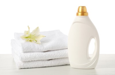 Photo of Bottle of fabric softener, stacked towels and flower on marble table against white background
