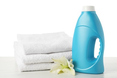 Photo of Bottle of fabric softener, stacked towels and flower on marble table against white background