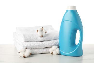 Photo of Bottle of fabric softener, stacked towels and cotton flowers on marble table against white background
