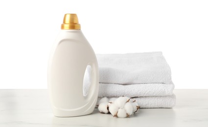 Photo of Bottle of fabric softener, stacked towels and cotton flowers on marble table against white background
