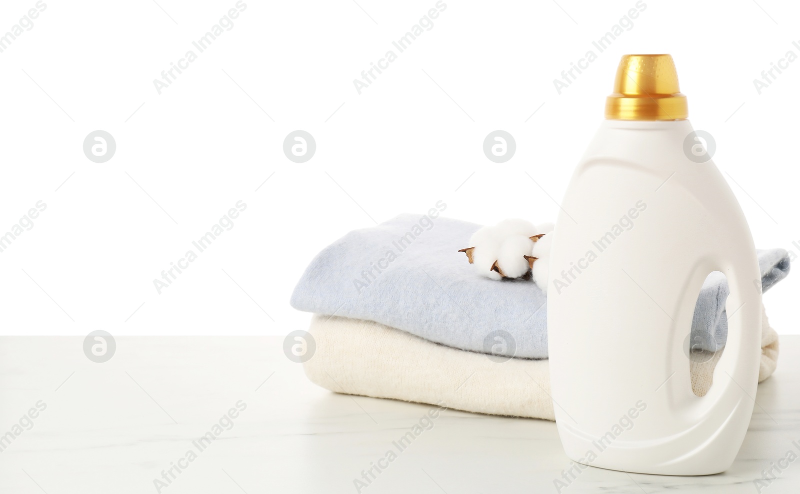 Bottle of fabric softener, stacked clothes and cotton flowers on marble table against white background Photo of Bottle of fabric softener, stacked clothes and cotton flowers on marble table against white background