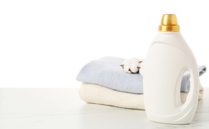 Photo of Bottle of fabric softener, stacked clothes and cotton flowers on marble table against white background