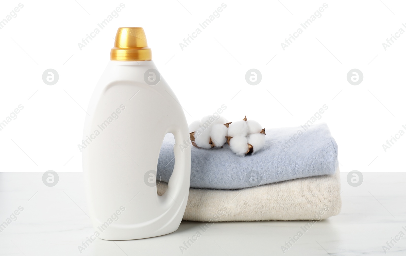 Bottle of fabric softener, stacked clothes and cotton flowers on marble table against white background Photo of Bottle of fabric softener, stacked clothes and cotton flowers on marble table against white background