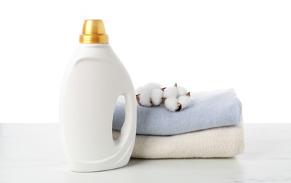 Photo of Bottle of fabric softener, stacked clothes and cotton flowers on marble table against white background