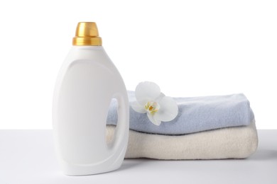 Photo of Bottle of fabric softener, stacked clothes and flower isolated on white