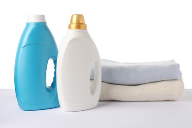 Photo of Bottles of fabric softener and stacked clothes isolated on white