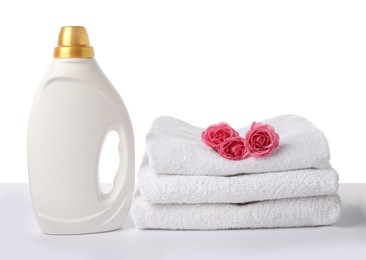 Photo of Bottle of fabric softener, stacked towels and flowers isolated on white